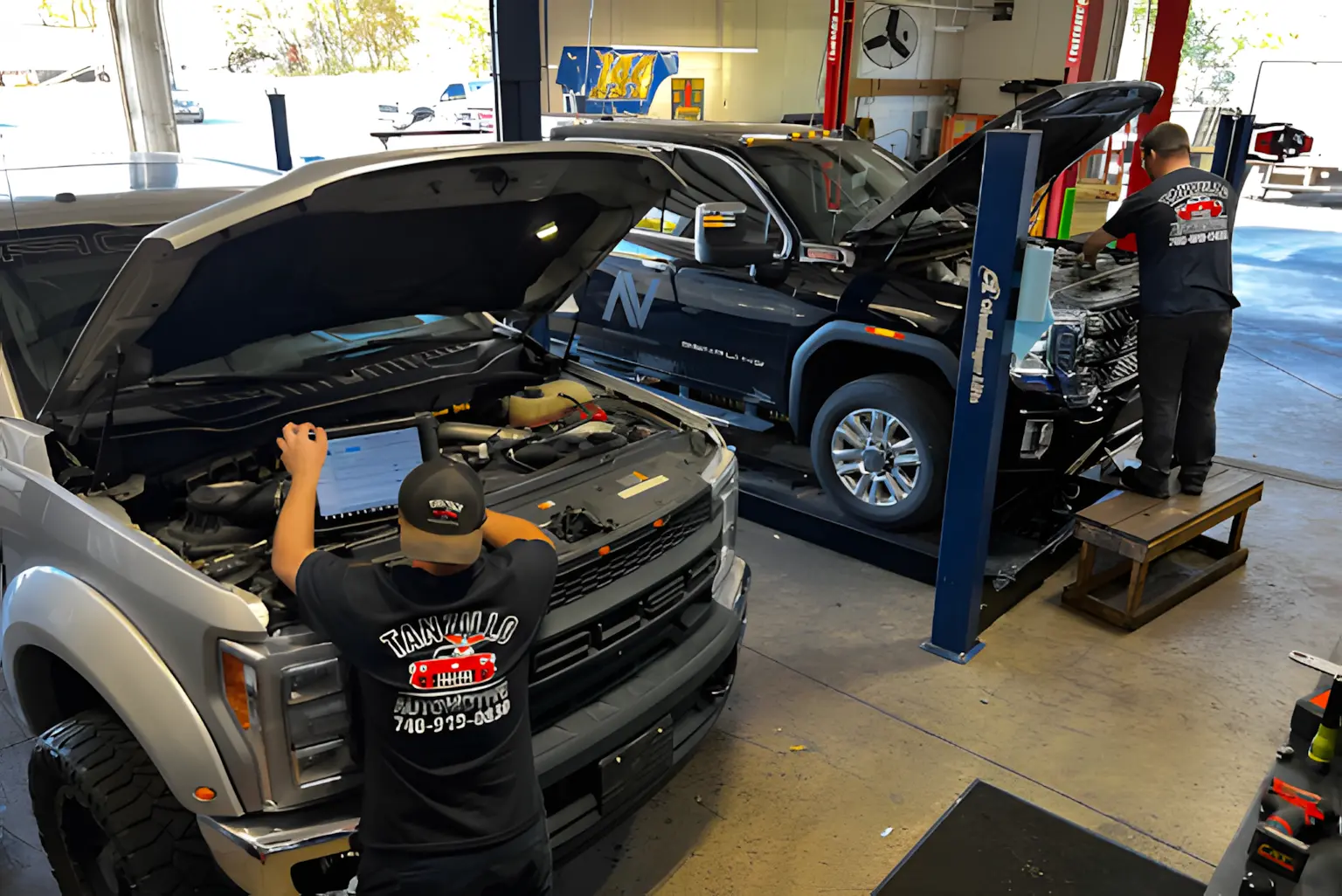 Auto repair mechanics at Tanzillo Automotive working on pickup trucks with hoods open for diagnostics and engine service.