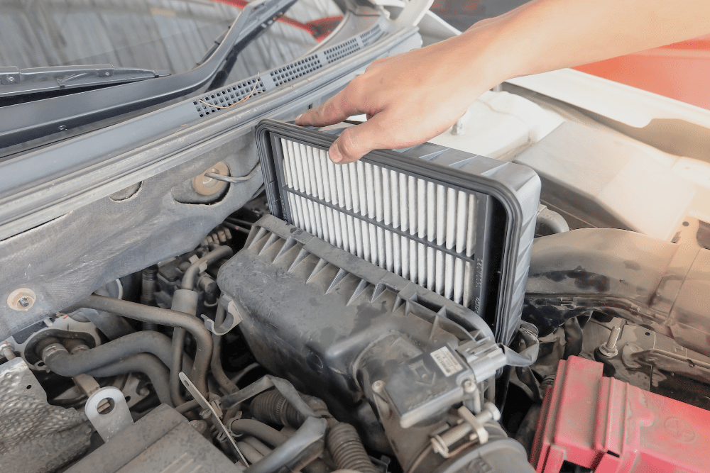 Engine Air Filter Replacement in Pataskala, OH At Tanzillo Automotive. A hand is performing an engine filter replacement in a car’s engine compartment, showing air filter maintenance work on the vehicle.