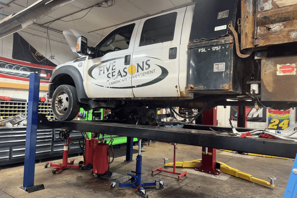 Fleet Maintenance in Pataskala, OH by Tanzillo Automotive: -- A white utility truck with is raised on a hydraulic lift in an auto repair shop for diesel engine maintenance