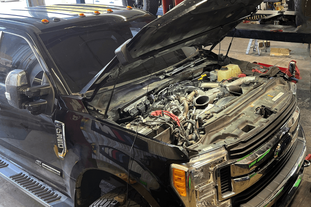DCR conversion, auto repair in Pataskala, OH, at Tanzillo Automotive. Image of a Ford Super Duty diesel truck with the hood open in a repair shop undergoing diesel engine service.